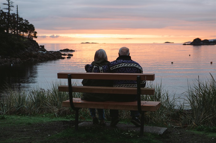 An elderly couple sits on a bench and looks out over Neck Point's waterfront