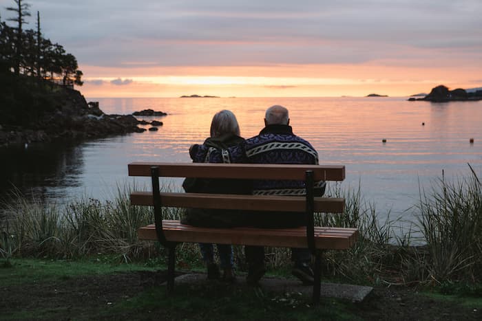 An elderly couple sits on a bench and looks out over Neck Point's waterfront