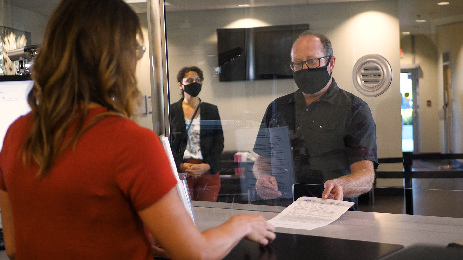 A man passes paperwork over to a City Worker at a business counter