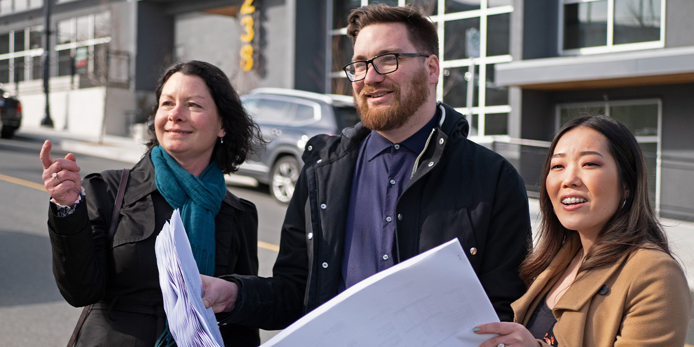 three young professionals are looking at a job site in the distance while holding blueprints