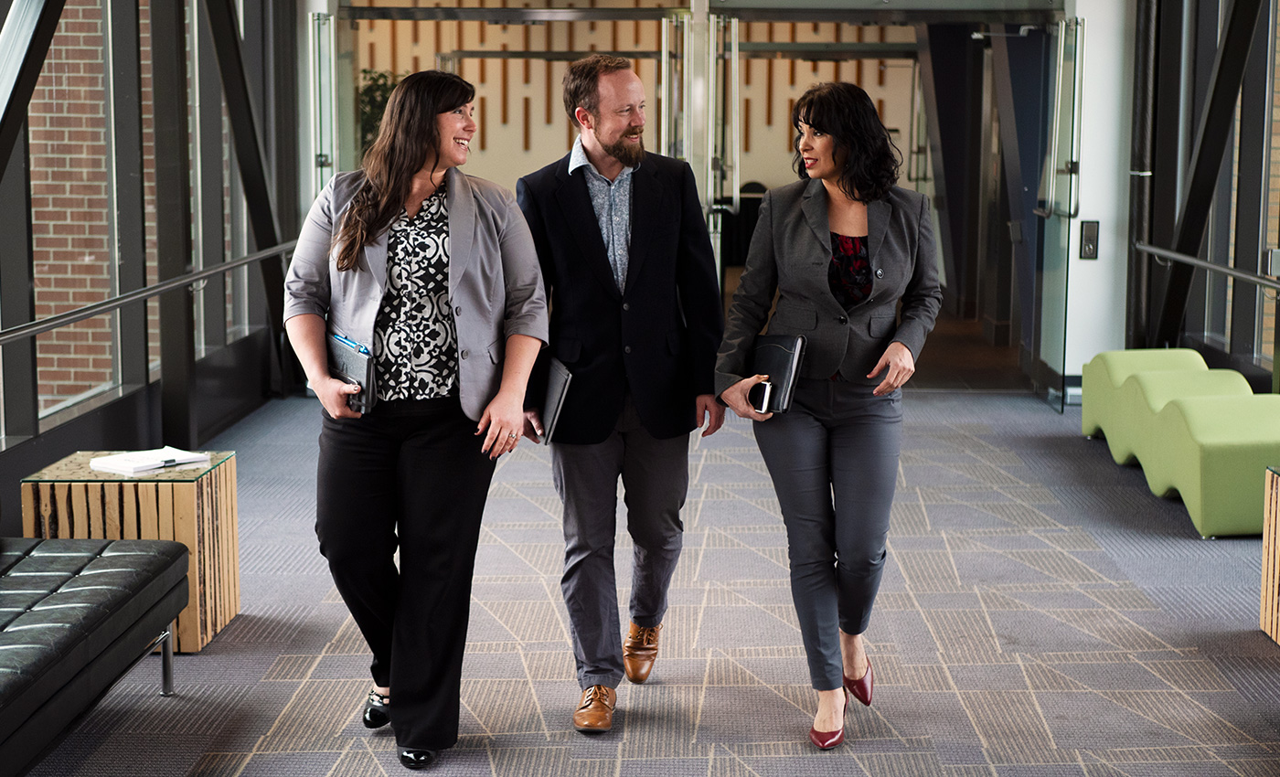 Three business professionals are walking a hallway and networking together