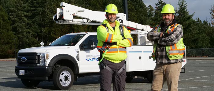 Two public works employees standing in front of their bucket truck