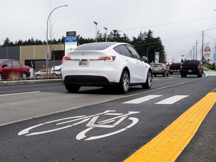 An electric car drives past the bike lane marking beside it.