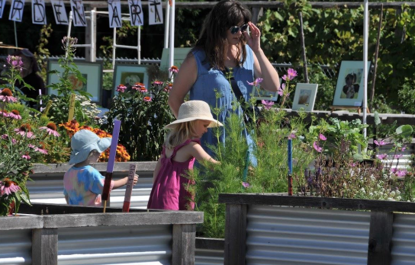 two small children and a woman standing between raised garden beds