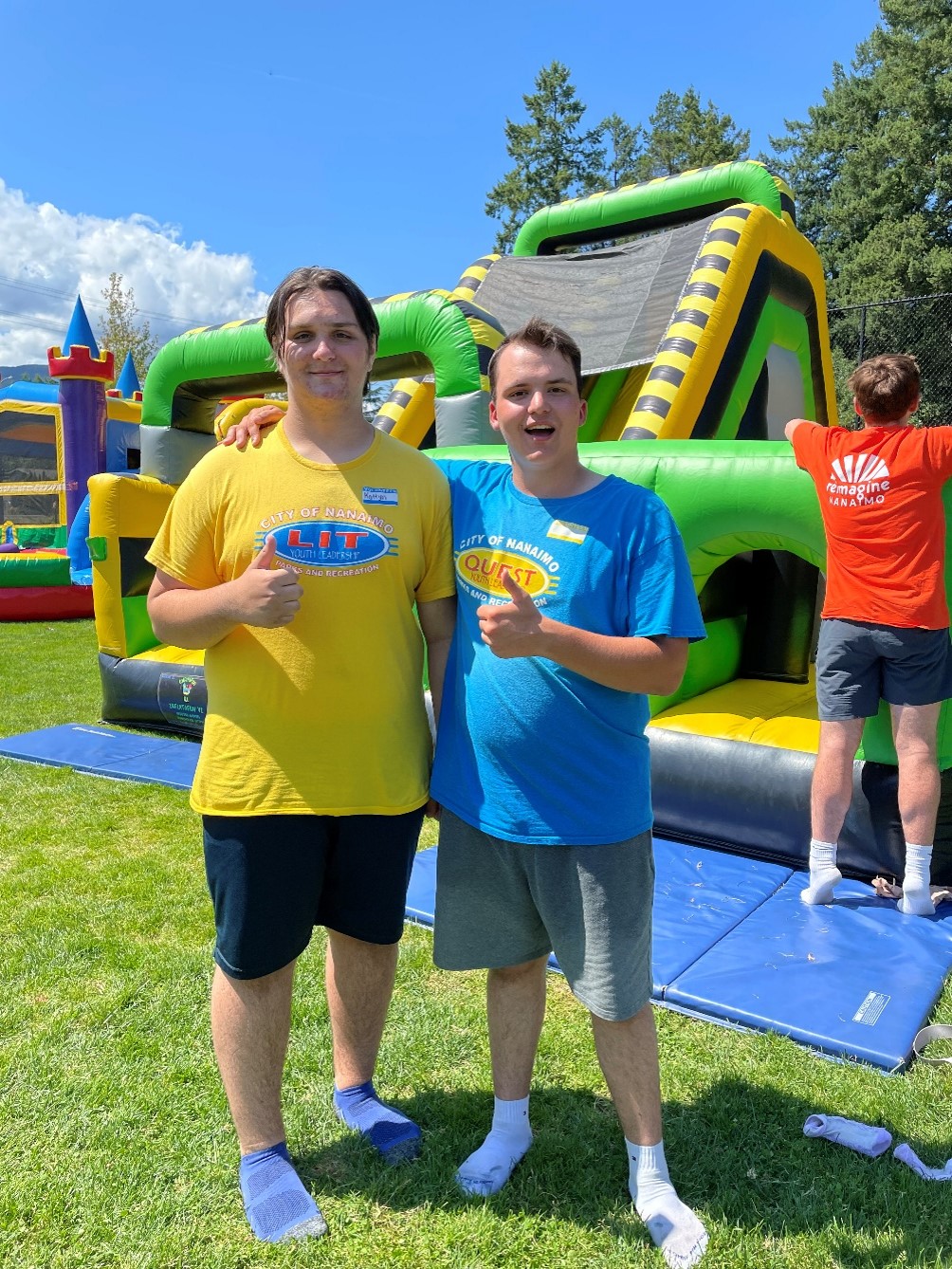 Quest leader and leader in training in front of a bouncy castle both giving a thumbs up.