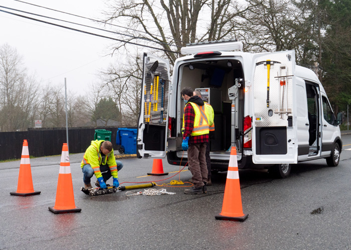 A small crew is monitoring the sewers at a service hatch with a CCTV van