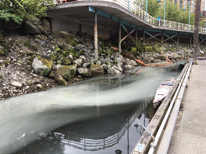 ConcreteslurrypollutingthewaterbeneathaconcretebridgespanningarockyshorelinewithamooredkayakbesideawalkwayintheNanaimoboatbasin