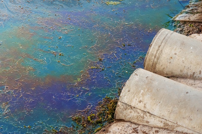 Sewerpipesatshorestainofoilorfuelonwatersurface