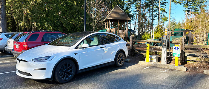 A white Tesla is plugged into a City of Nanaimo EV Charger at Oliver Woods Park