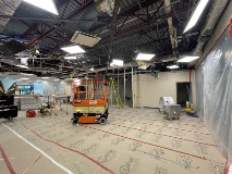 Scissorliftinthecenterofaroomwithexposedstructureattheceilingkraftpaperonthefloorandplasticsheetingontherightandleft
